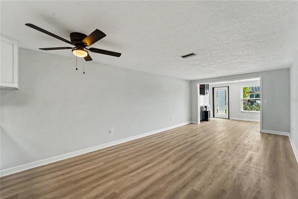 A living room with light gray walls, wood-look flooring, a ceiling fan, and an entryway — 4247 STRATFORD DRIVE, NEW PORT RICHEY, FL