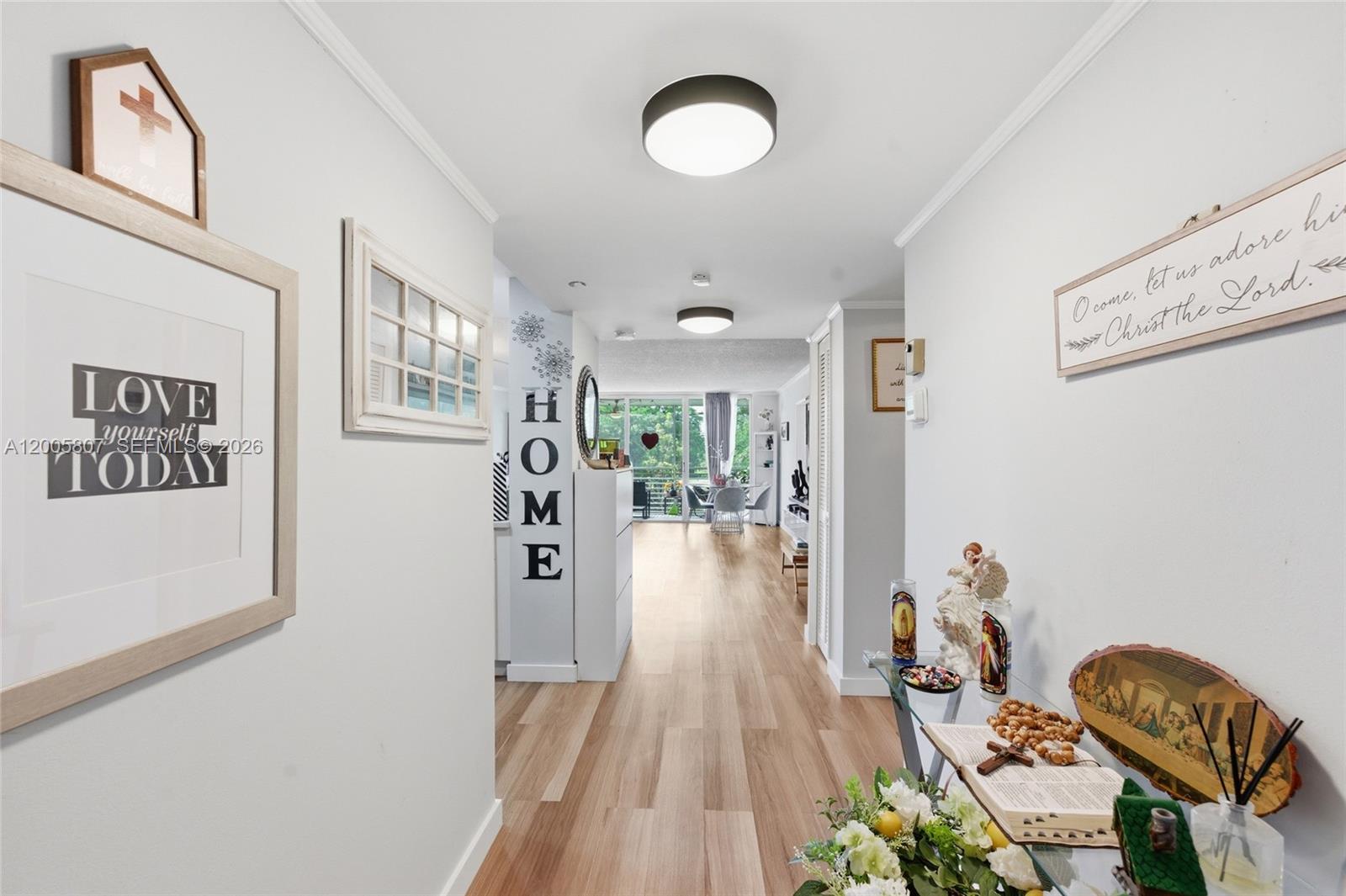 A hallway with light wood flooring leads toward a bright living area with balcony access — 625 Oaks Dr # 304, Pompano Beach FL 33069, POMPANO BEACH, FL
