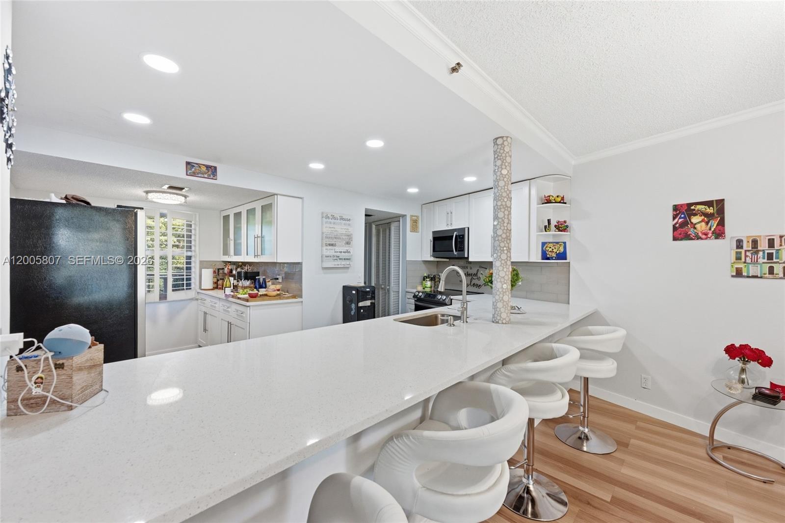 A kitchen features white cabinetry, a long quartz breakfast bar, and three white barstools — 625 Oaks Dr # 304, Pompano Beach FL 33069, POMPANO BEACH, FL