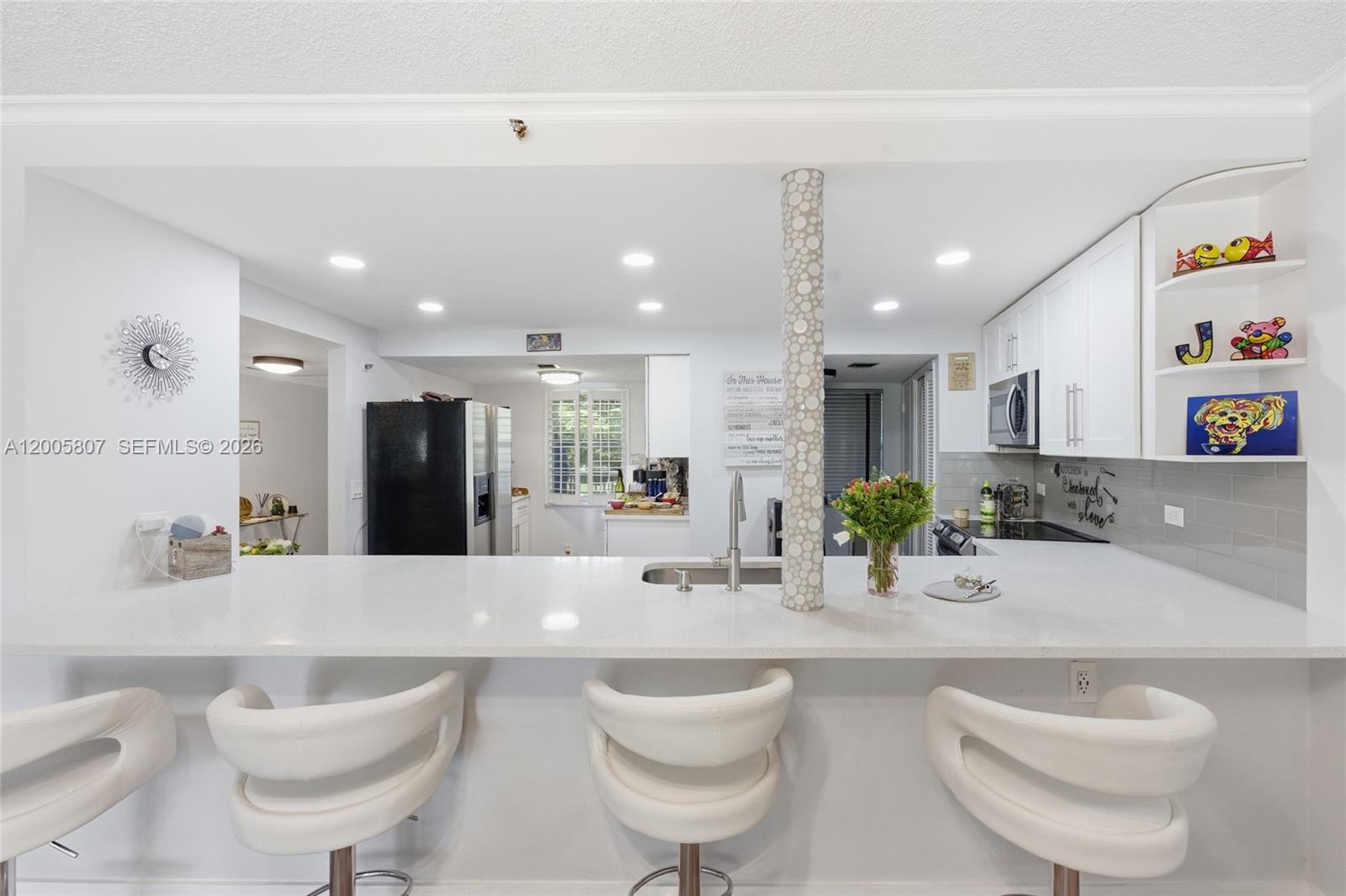 A kitchen features a white breakfast bar with three stools and a decorative mosaic column — 625 Oaks Dr # 304, Pompano Beach FL 33069, POMPANO BEACH, FL