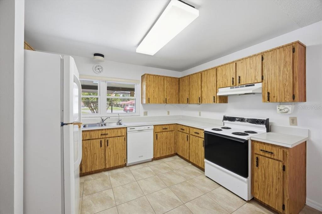 A kitchen features wood-grain cabinets, white appliances, tile flooring, and a large rectangular ceiling light — 535 HUNTER CIRCLE UNIT 535, KISSIMMEE, FL