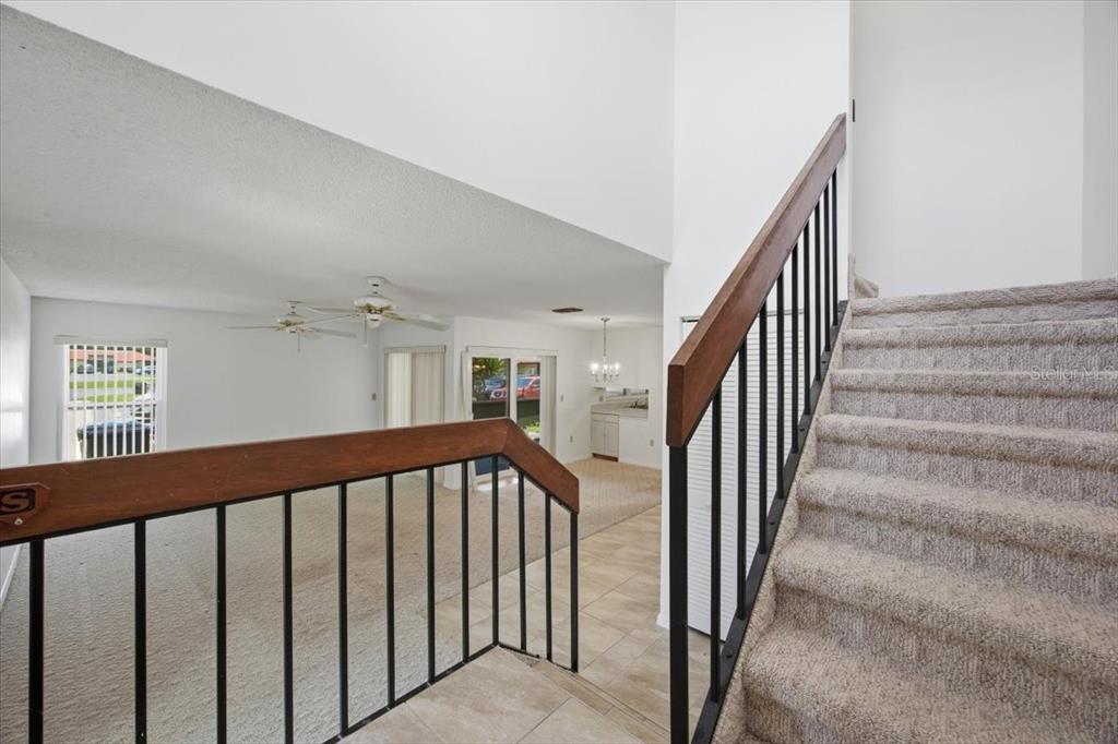 A carpeted staircase with a wooden handrail overlooks a living area with tile flooring — 535 HUNTER CIRCLE UNIT 535, KISSIMMEE, FL
