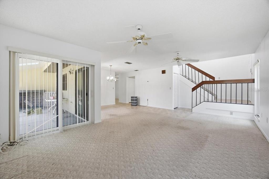 A living room with beige carpet, white walls, ceiling fans, and a staircase with railings — 535 HUNTER CIRCLE UNIT 535, KISSIMMEE, FL