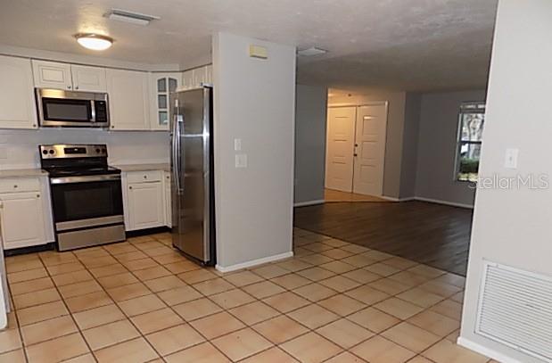 A kitchen with white cabinets, stainless steel appliances, and tile flooring opens to a living area — 2173 FIESTA DRIVE, SARASOTA, FL