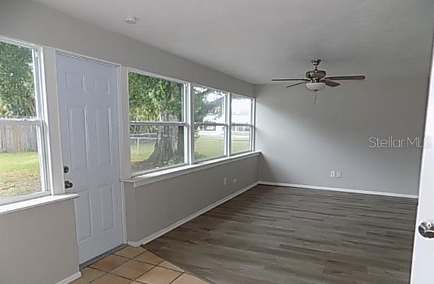 A sunroom features light gray walls, wood-look flooring, a ceiling fan, and large windows — 2173 FIESTA DRIVE, SARASOTA, FL