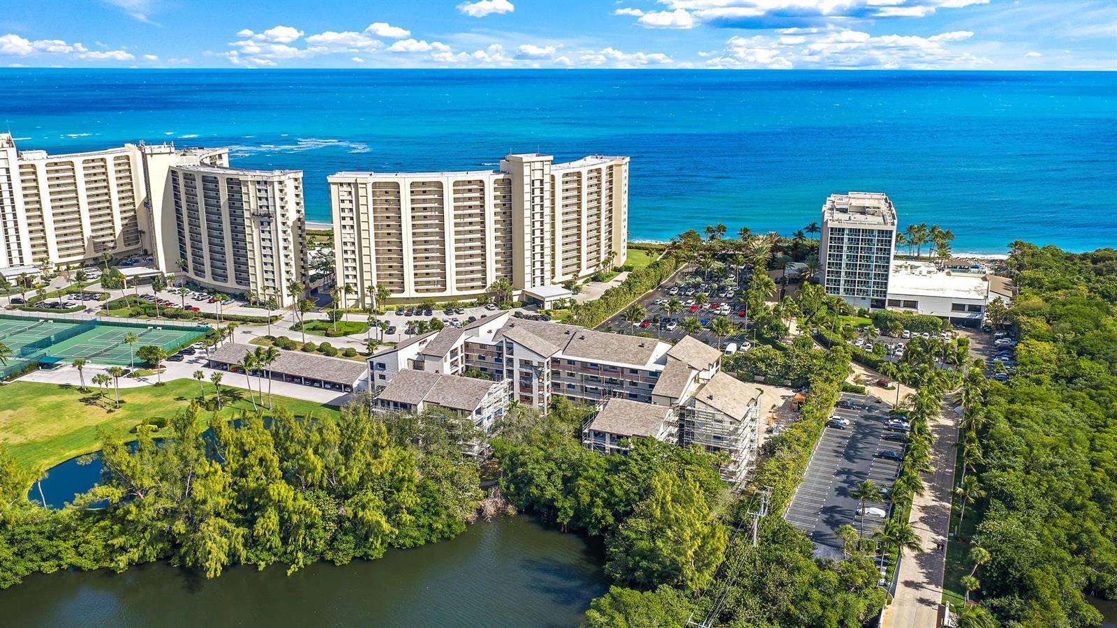 An aerial view shows several multi-story apartment buildings near a beach and a lake — 500 Ocean Trail Way # 305, Jupiter FL 33477, JUPITER, FL