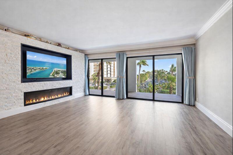 A living room features a stone fireplace, a wall-mounted television, and large sliding glass doors — 500 Ocean Trail Way # 305, Jupiter FL 33477, JUPITER, FL