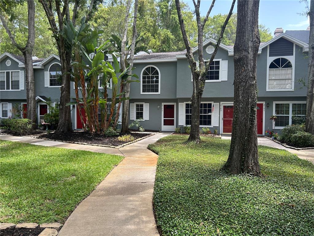 A row of gray townhouses with red doors and arched windows sits behind a paved walkway — 2143 FOX CHASE BOULEVARD, PALM HARBOR, FL