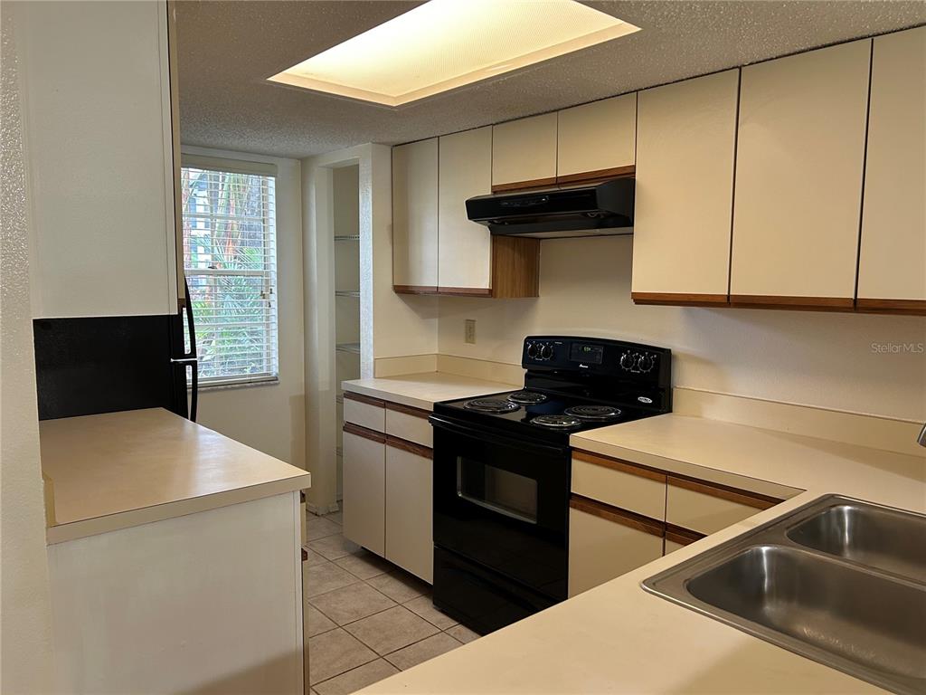 A kitchen features white cabinets, black appliances, light countertops, and a window with blinds — 2143 FOX CHASE BOULEVARD, PALM HARBOR, FL
