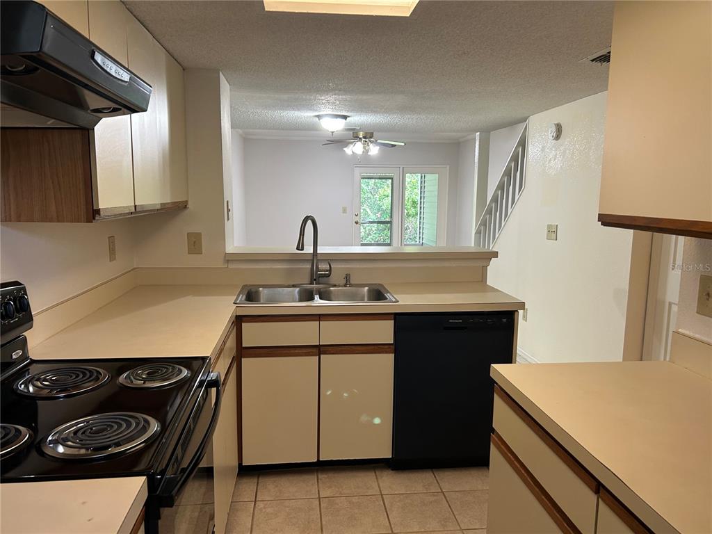 A kitchen with beige countertops, white cabinets, and a black dishwasher overlooks a living area — 2143 FOX CHASE BOULEVARD, PALM HARBOR, FL