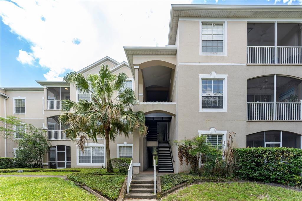A three-story apartment building exterior features a central staircase, screened balconies, and a palm tree — 1212 S HIAWASSEE ROAD UNIT 525, ORLANDO, FL