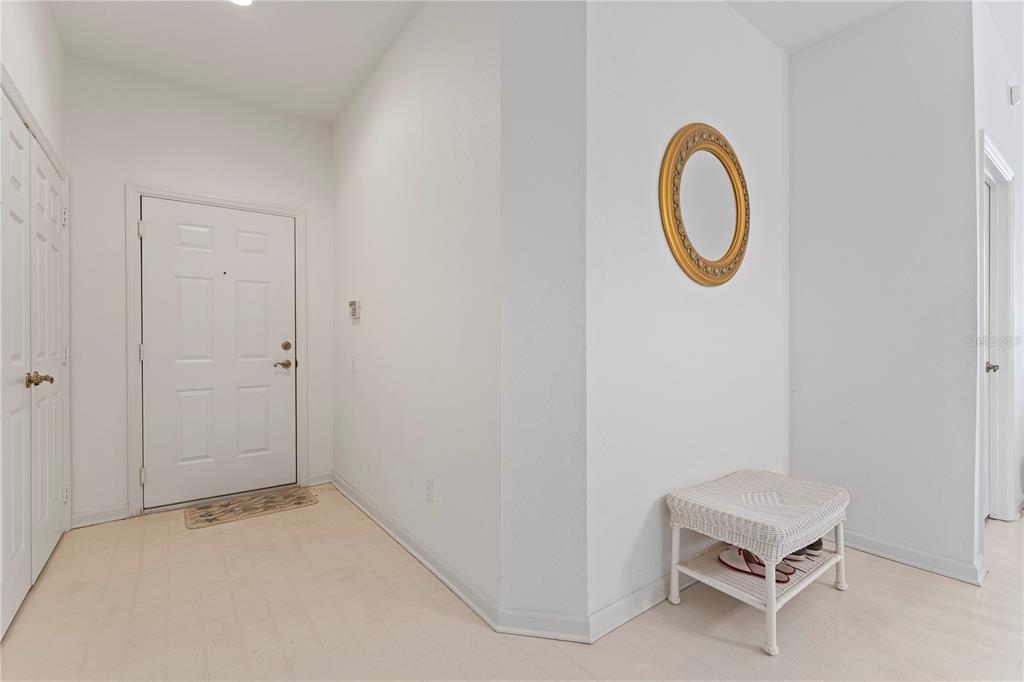 An entryway features a white door, a gold-framed oval mirror, and a small wicker bench — 1212 S HIAWASSEE ROAD UNIT 525, ORLANDO, FL