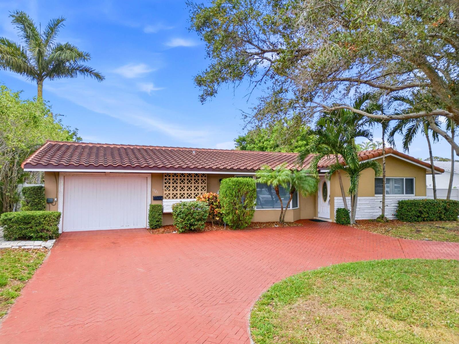 A single-story house with a red tile roof, white garage door, and red brick driveway — 1921 NE 28th Court, Lighthouse Point FL 33064, LIGHTHOUSE POINT, FL