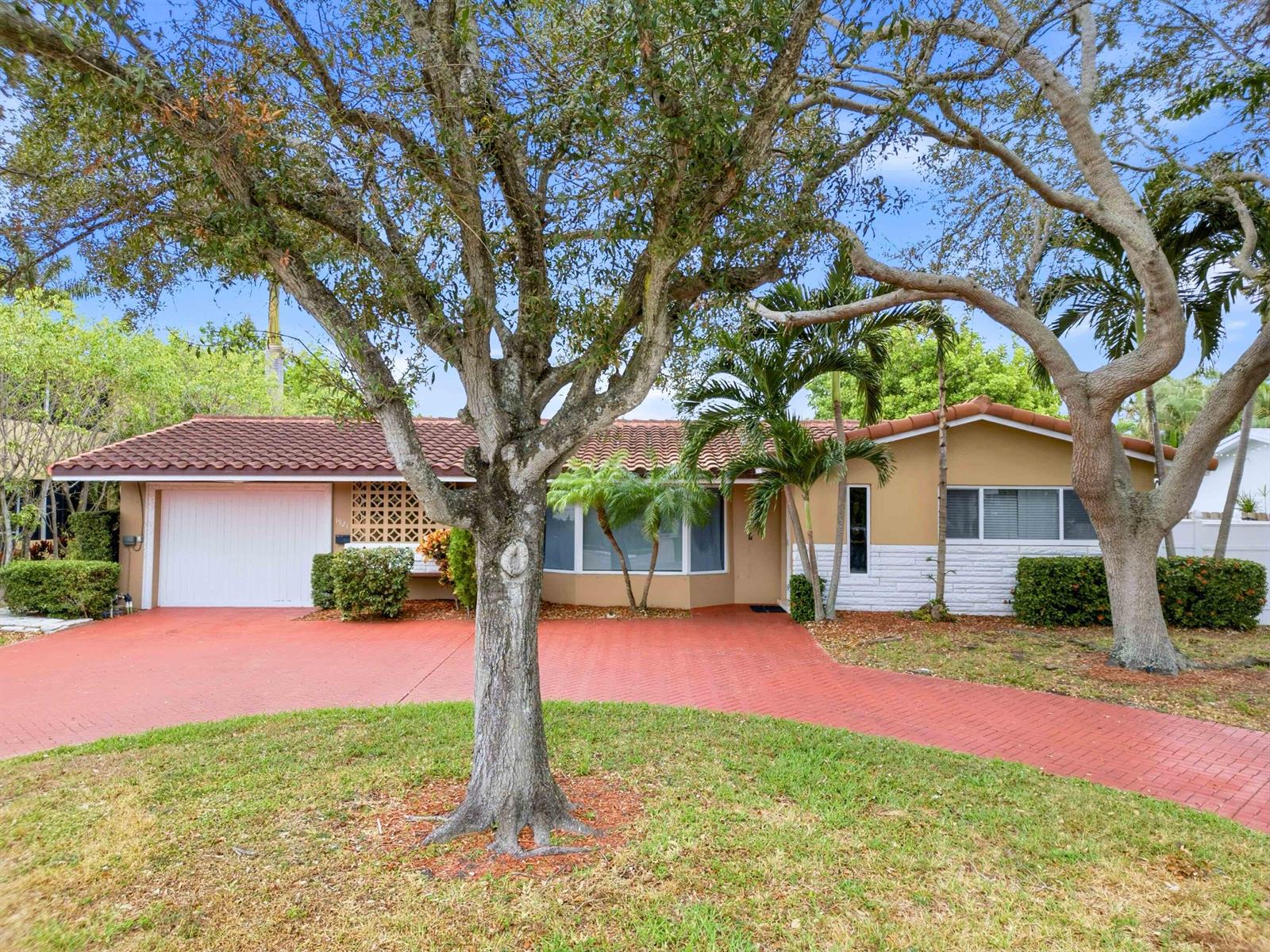 A single-story house with a red brick driveway, a tiled roof, and large shade trees — 1921 NE 28th Court, Lighthouse Point FL 33064, LIGHTHOUSE POINT, FL