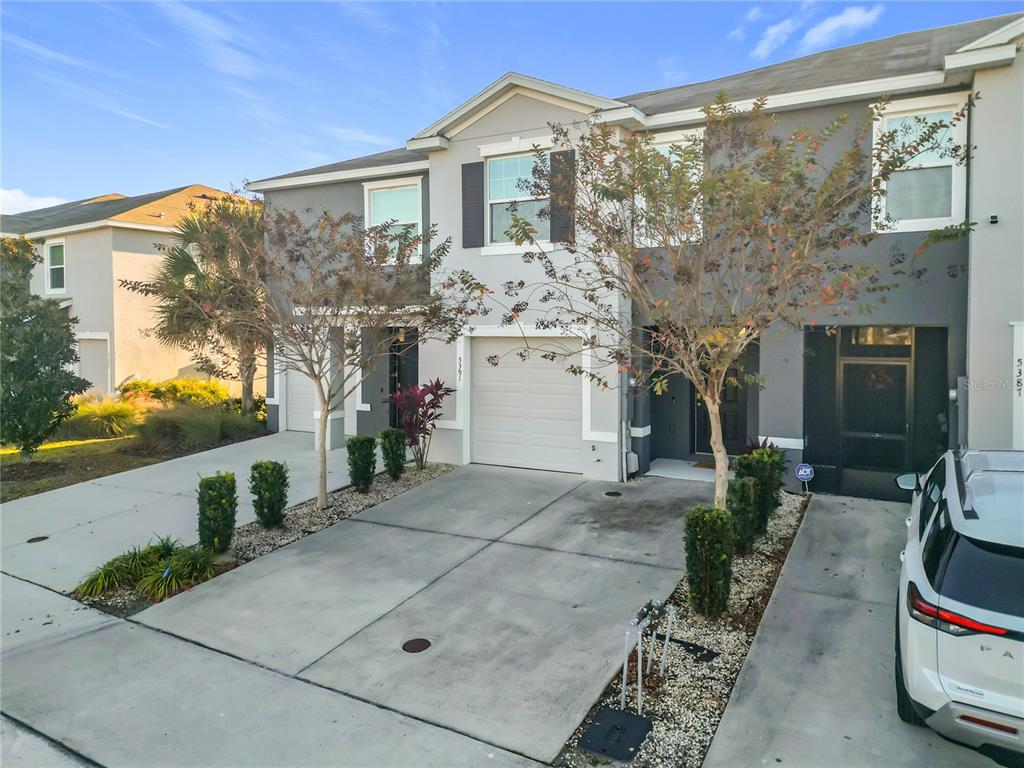 An exterior view of a two-story townhouse with a concrete driveway and small front landscaping — 5391 DRAGONFLY DRIVE, WILDWOOD, FL