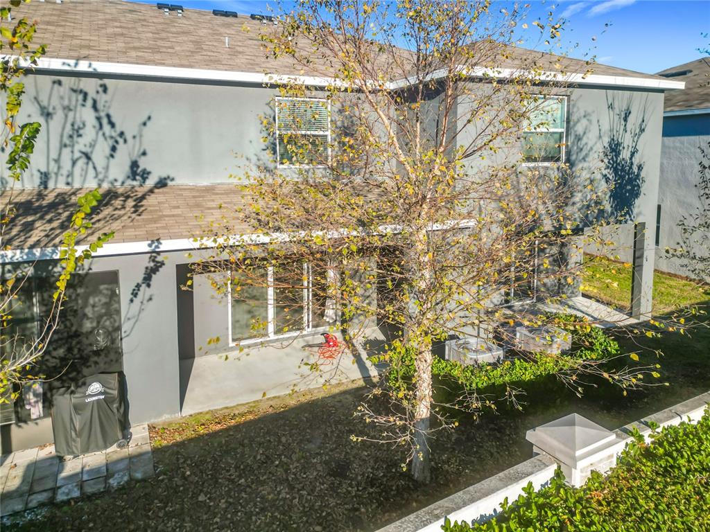 The exterior rear view of a two-story gray house with a small patio and tree — 5391 DRAGONFLY DRIVE, WILDWOOD, FL