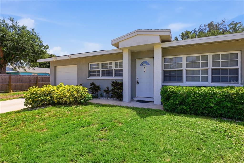 A single-story house with a white front door, a garage, and green landscaping — 910 16TH AVENUE W, PALMETTO, FL
