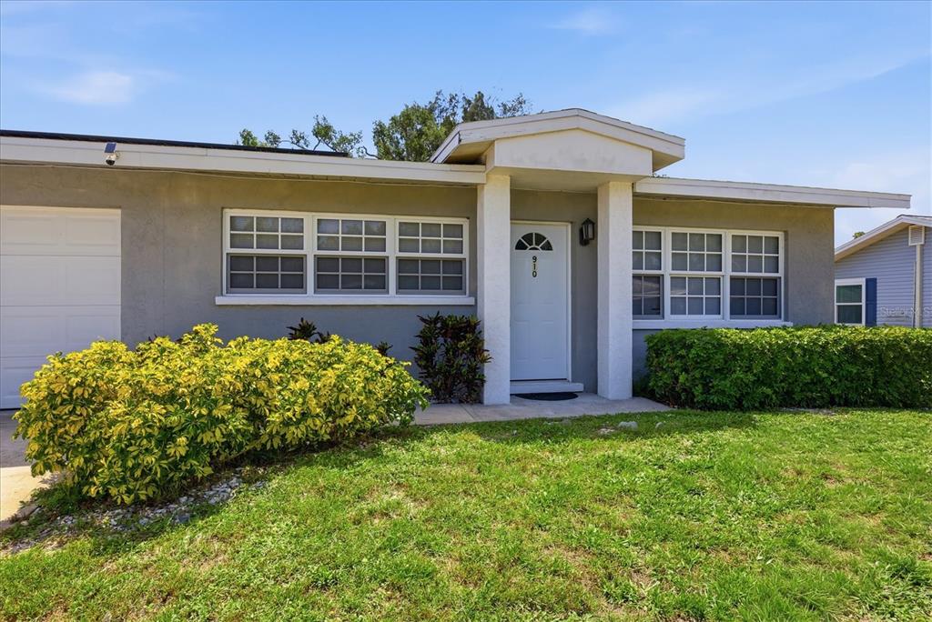 A single-story house exterior features a white front door, gray siding, and a manicured lawn — 910 16TH AVENUE W, PALMETTO, FL