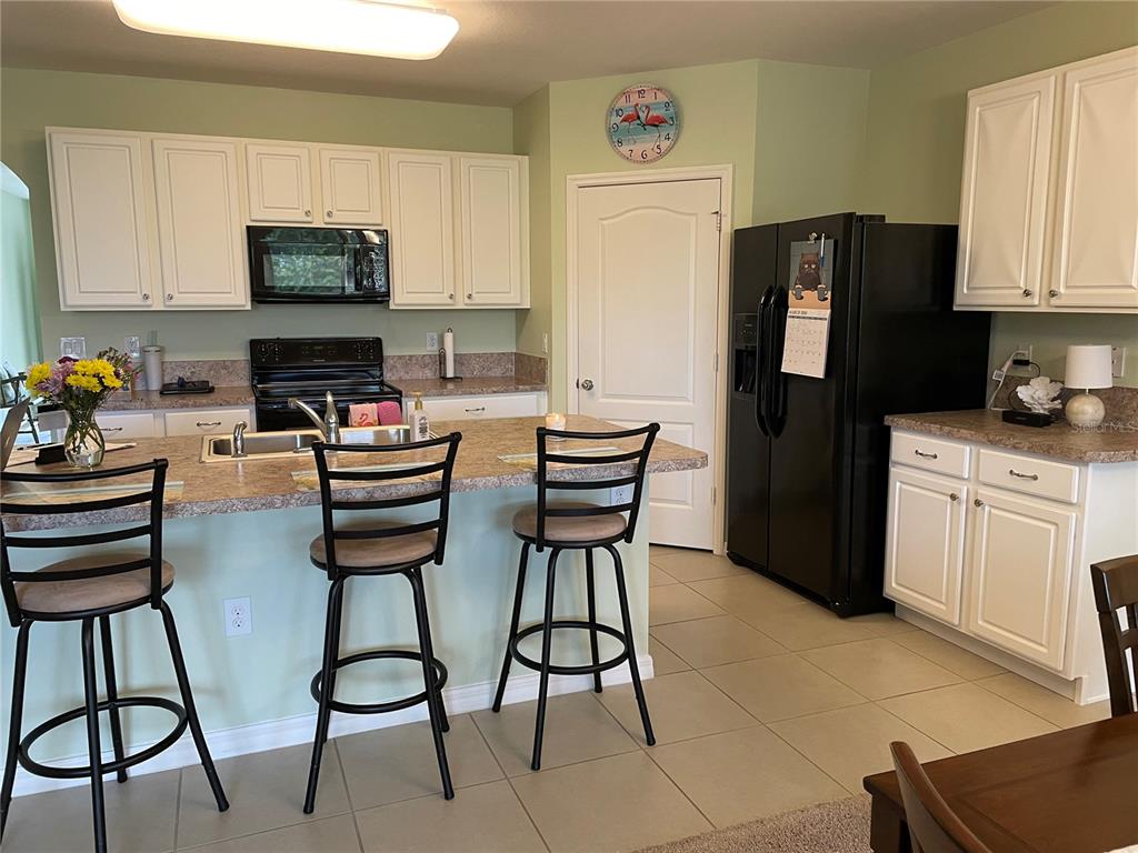 A kitchen with white cabinets, a granite island, black appliances, and three bar stools — 119 FISHERMANS COVE DRIVE, EDGEWATER, FL