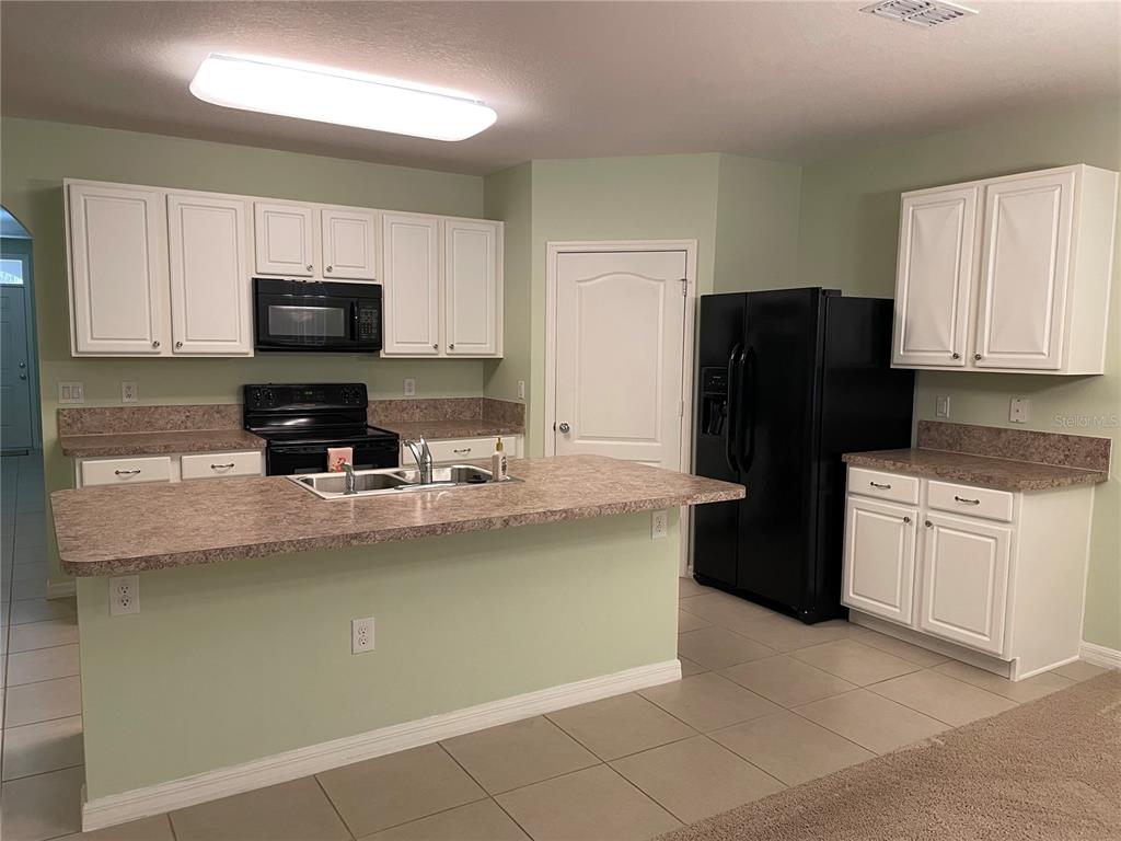 A kitchen features white cabinets, black appliances, a laminate countertop island, and light green walls — 119 FISHERMANS COVE DRIVE, EDGEWATER, FL