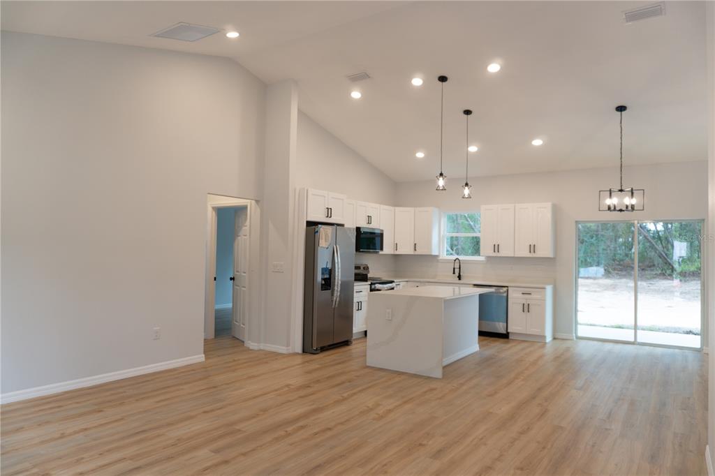 A modern kitchen with white cabinets, a center island, and wood-look flooring in an open-concept space — 16 HEMLOCK TRL, OCALA, FL