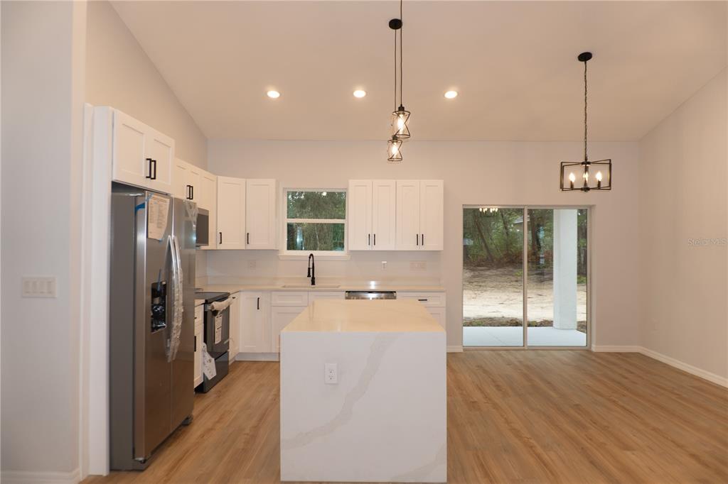 A modern kitchen features white cabinets, a quartz island, stainless steel appliances, and wood flooring — 16 HEMLOCK TRL, OCALA, FL
