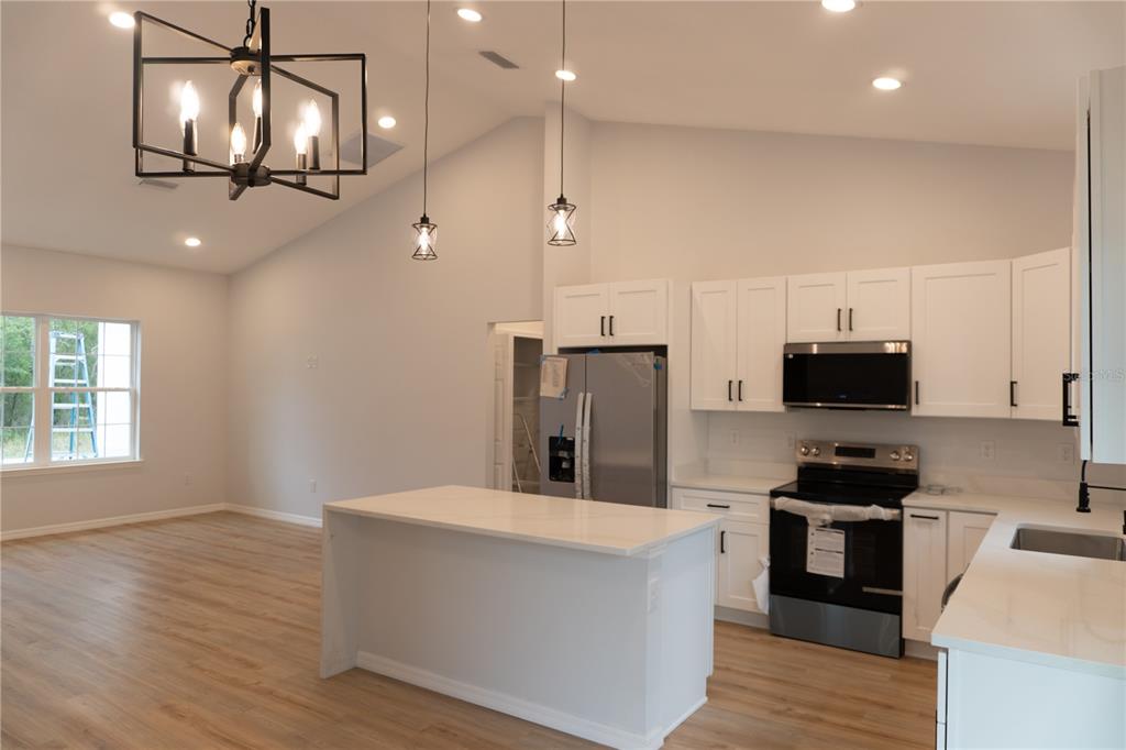 A kitchen with white cabinets, stainless steel appliances, a center island, and wood-look flooring — 16 HEMLOCK TRL, OCALA, FL