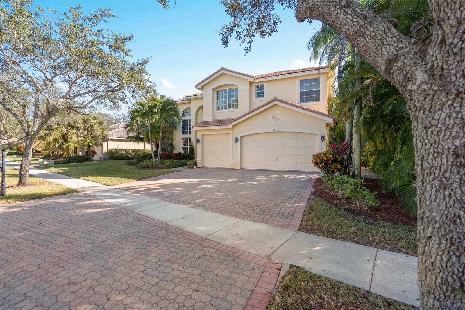 A two-story, light-yellow suburban house features a three-car garage and a paved driveway — 19434 Estuary Drive, Boca Raton FL 33498, BOCA RATON, FL