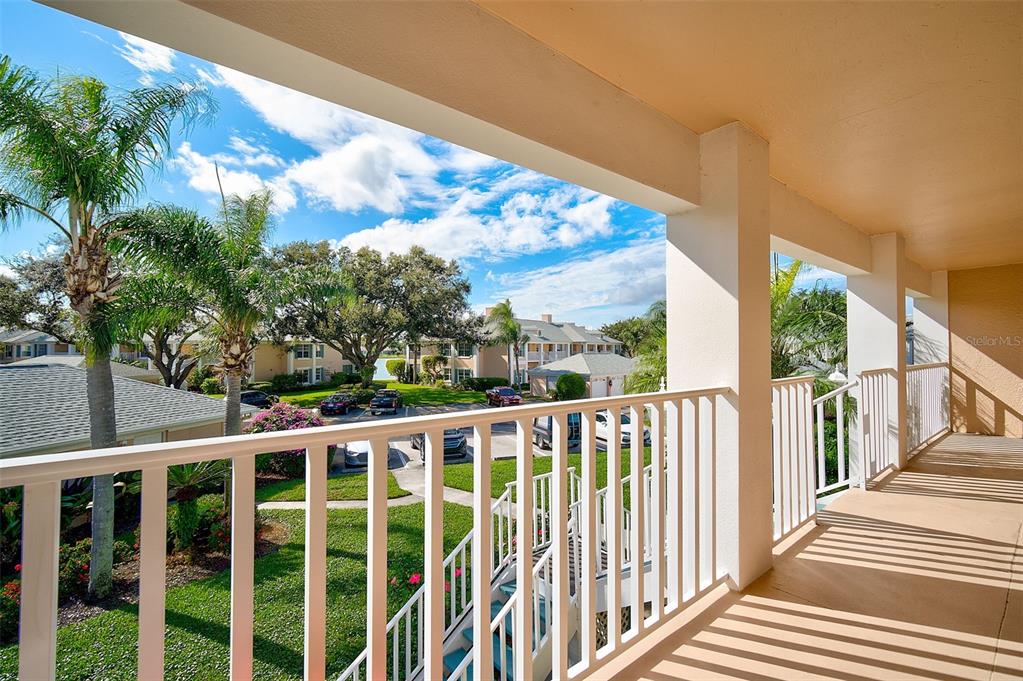A covered balcony with white railings overlooks a parking lot, palm trees, and apartment buildings — 4706 SAND TRAP STREET CIRCLE E UNIT 202, BRADENTON, FL