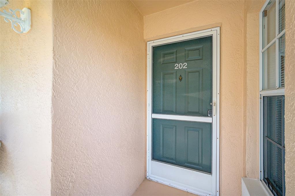 A front entrance with a screen door labeled 202, beige stucco walls, and a window — 4706 SAND TRAP STREET CIRCLE E UNIT 202, BRADENTON, FL