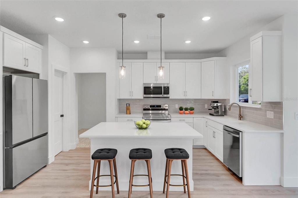 A modern kitchen features white cabinetry, a central island with bar stools, and stainless appliances — Lot #21 KAROLINA AVE, WINTER PARK, FL