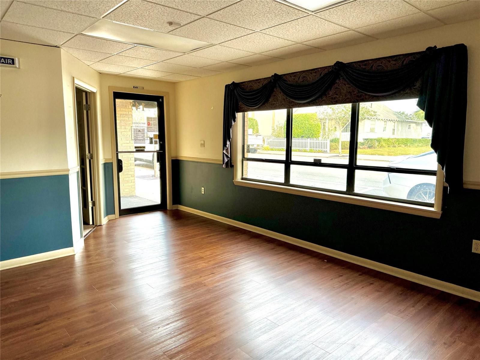 An empty office space features wood-look flooring, dark teal wainscoting, and a large window — 145 S Ridgewood Drive, Sebring FL 33870, SEBRING, FL