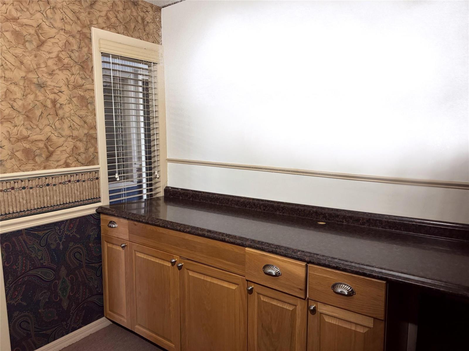 A room features oak cabinets with a dark countertop, patterned wallpaper, and a window with blinds — 145 S Ridgewood Drive, Sebring FL 33870, SEBRING, FL