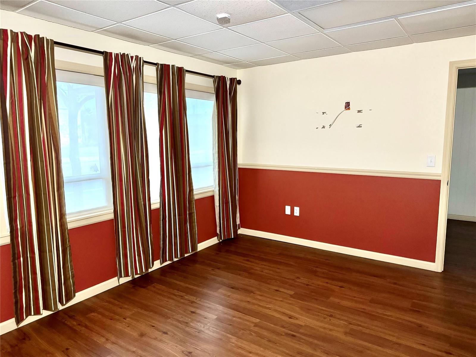 An empty room features wood-look flooring, red wainscoting, striped curtains, and a drop ceiling — 145 S Ridgewood Drive, Sebring FL 33870, SEBRING, FL