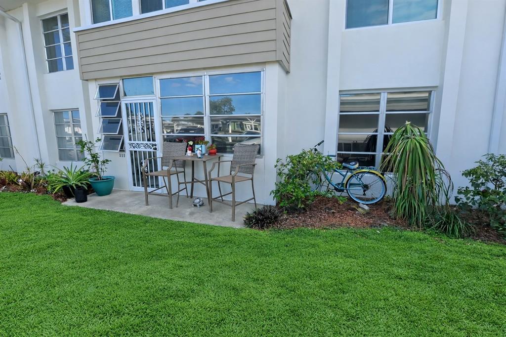 A ground-level patio with a table and chairs sits outside a building with large windows — 21300 BRINSON AVENUE UNIT 111, PORT CHARLOTTE, FL