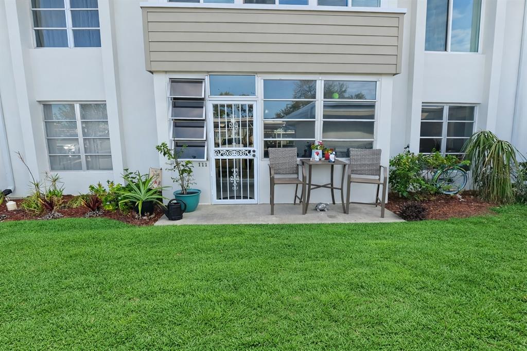 A ground-level patio with two chairs and a small table sits outside a glass door — 21300 BRINSON AVENUE UNIT 111, PORT CHARLOTTE, FL
