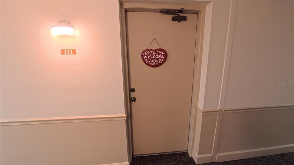 A beige apartment door labeled 111 features a heart-shaped welcome sign in a hallway — 21300 BRINSON AVENUE UNIT 111, PORT CHARLOTTE, FL