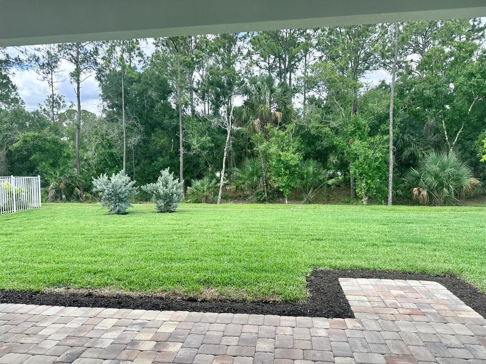 A view of a backyard with a paver patio, green lawn, and surrounding trees — 4425 SW Cornerstone Way # 169, Stuart FL 34997, STUART, FL