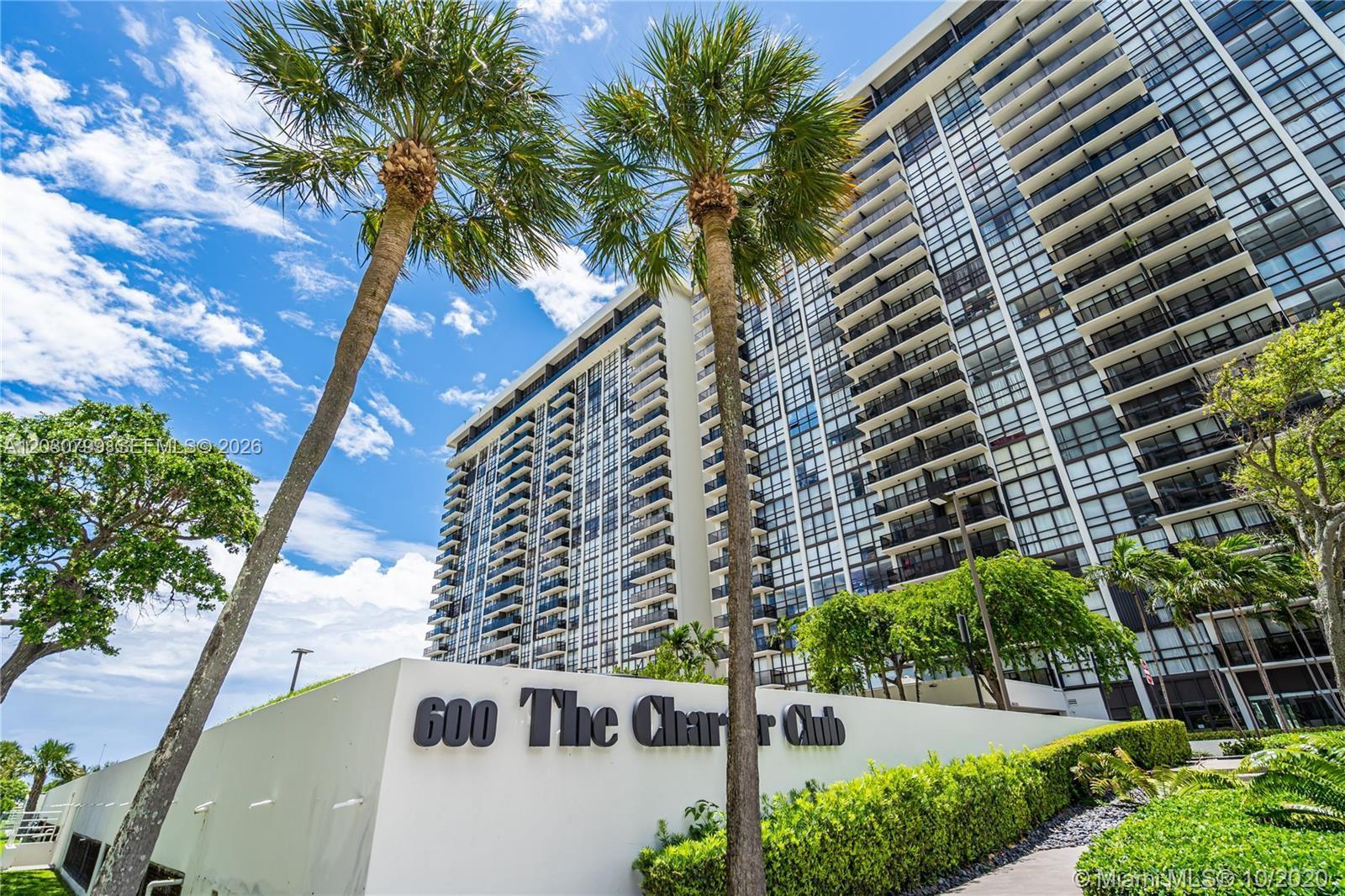 A tall residential building stands behind a white wall labeled 600 The Charter Club — 600 NE 36th St # 417, Miami FL 33137, MIAMI, FL