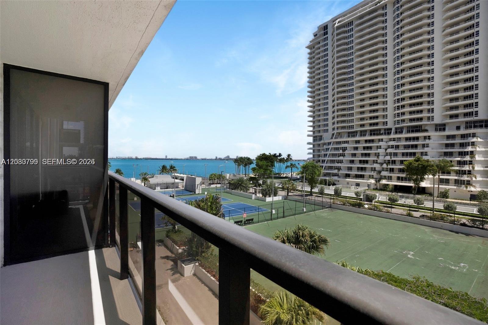 A balcony overlooks tennis courts, a large residential building, and a body of water — 600 NE 36th St # 417, Miami FL 33137, MIAMI, FL