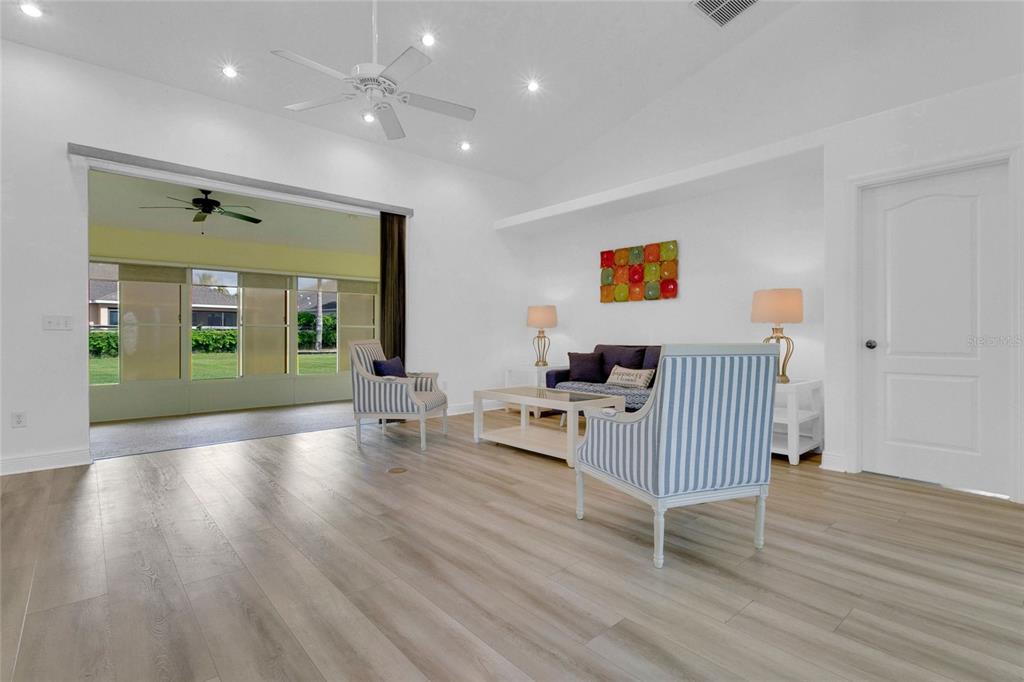 A living room features light wood-look flooring, white walls, two striped chairs, and a sofa — 5433 COUNTY ROAD 125, WILDWOOD, FL