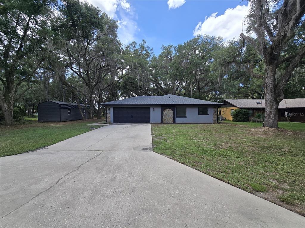 A gray single-story house with a dark garage door and stone accents sits on a lot — 3512 SW SHOREWOOD DRIVE, DUNNELLON, FL
