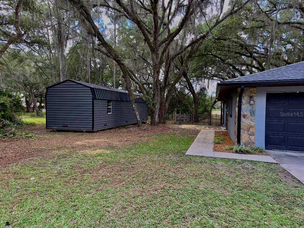 A dark gray shed sits on a grassy lawn next to a house with stone siding — 3512 SW SHOREWOOD DRIVE, DUNNELLON, FL