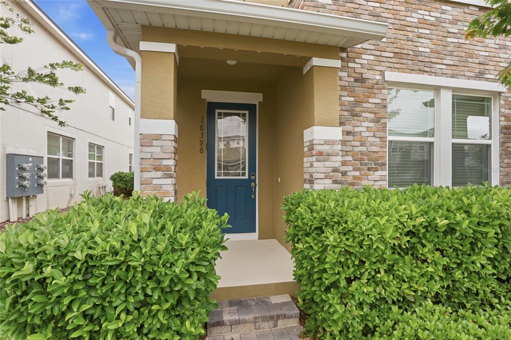 A blue front door with a glass insert is framed by stone pillars and hedges — 16396 PRAIRIE SCHOOL DRIVE, WINTER GARDEN, FL