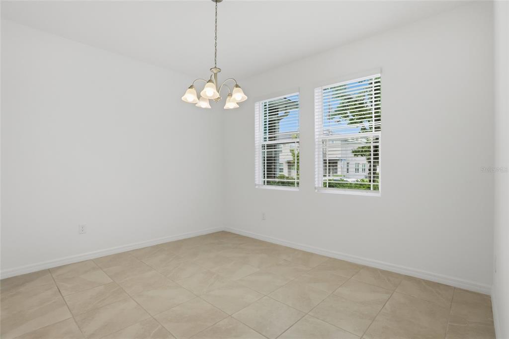 An empty dining room features white walls, tile flooring, a chandelier, and two windows — 16396 PRAIRIE SCHOOL DRIVE, WINTER GARDEN, FL
