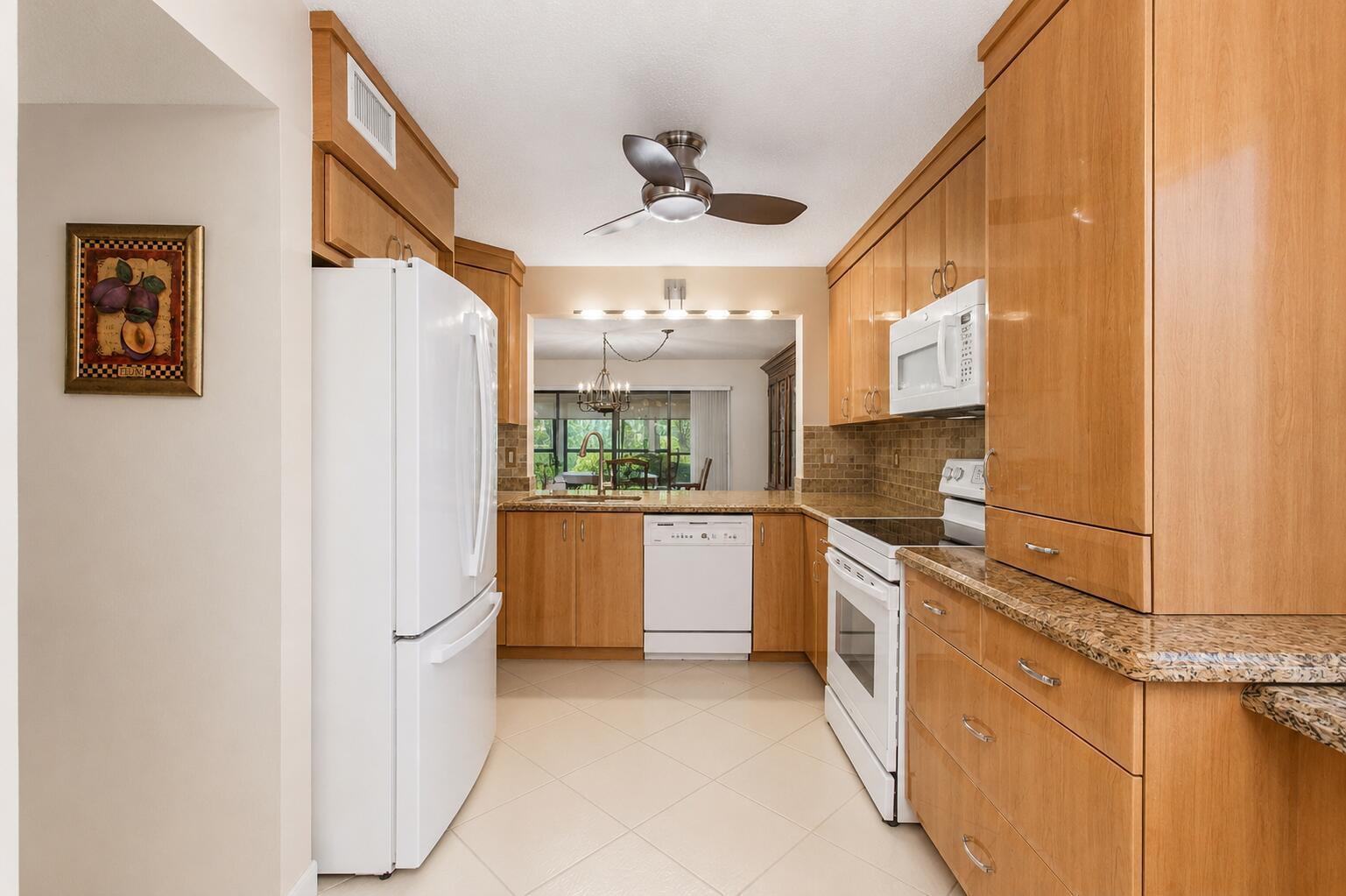 A kitchen with light wood cabinets, granite countertops, white appliances, and a ceiling fan — 5561 Fairway Park Drive # 104, Boynton Beach FL 33437, BOYNTON BEACH, FL