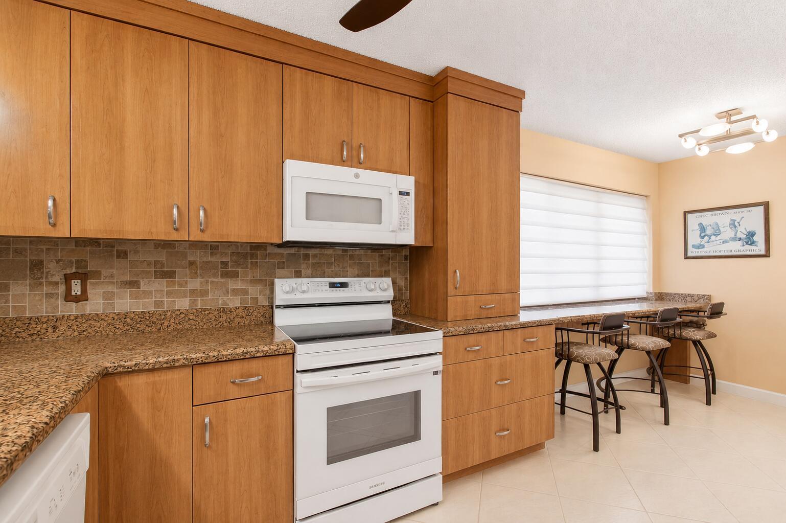 A kitchen features wood cabinets, granite countertops, a white stove, and a breakfast bar area — 5561 Fairway Park Drive # 104, Boynton Beach FL 33437, BOYNTON BEACH, FL