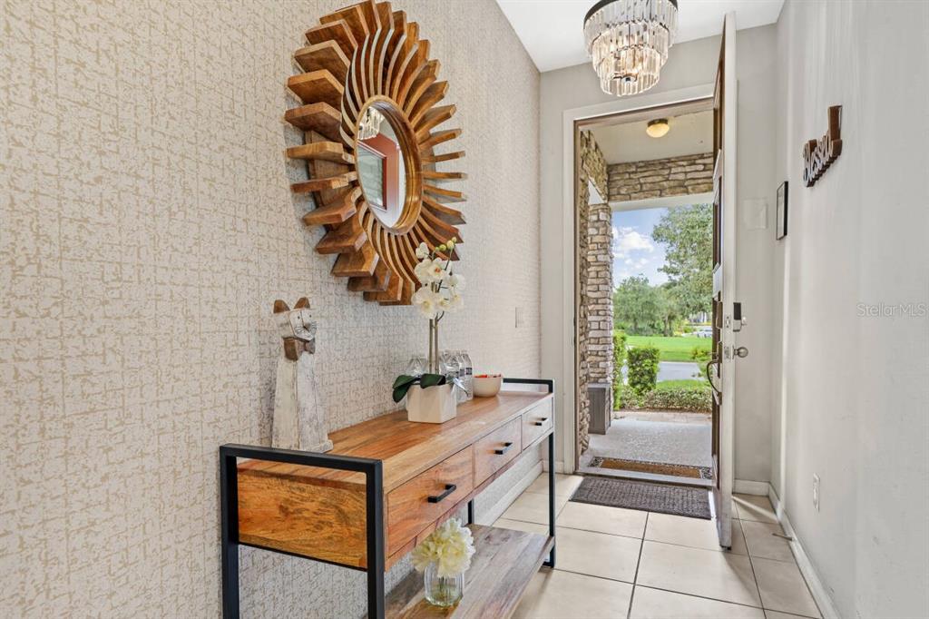 An entryway features a wooden console table, a sunburst mirror, and an open front door — 1804 SANDY PARK TRAIL, KISSIMMEE, FL