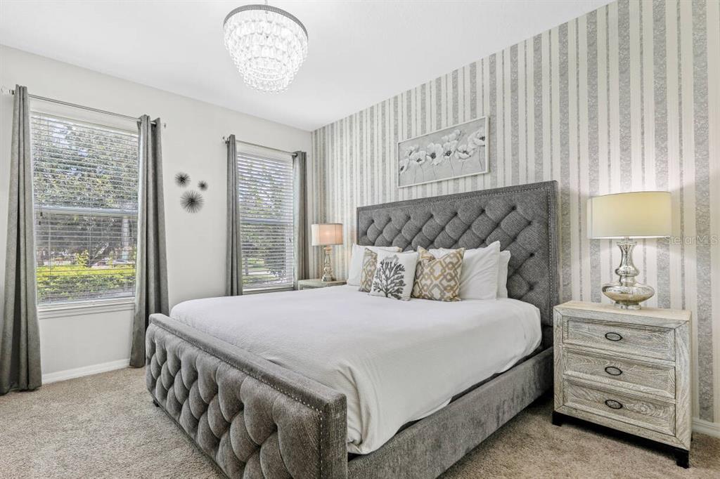 A bedroom features a tufted gray bed, striped wallpaper, and a crystal chandelier — 1804 SANDY PARK TRAIL, KISSIMMEE, FL