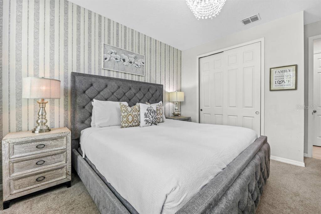 A bedroom features a tufted gray bed, striped wallpaper, and a white closet door — 1804 SANDY PARK TRAIL, KISSIMMEE, FL